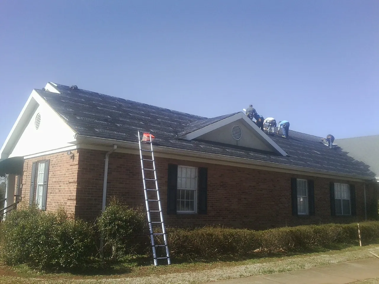 Crew tearing shingles off a brick ranch roof with a ladder set — Metal Roof Repair work by our crew in Palmyra